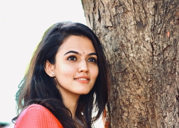 Aparna Das standing against a tree in red dress
