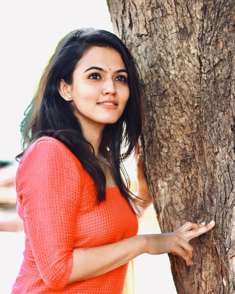 Aparna Das standing against a tree in red dress