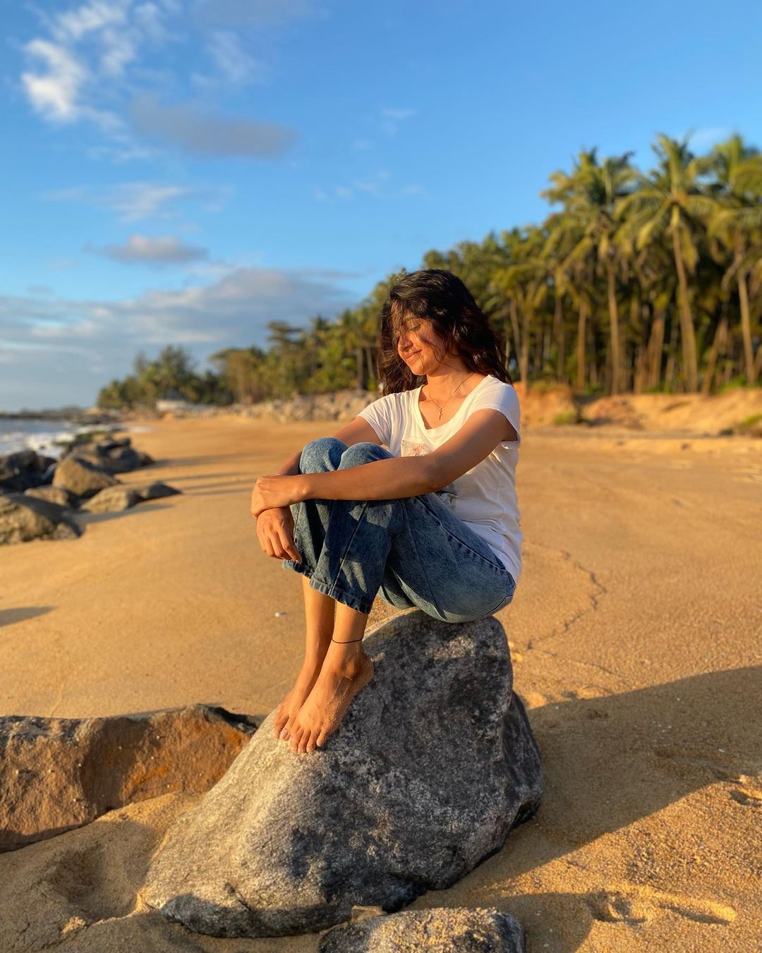 Kushee Ravi sitting on a rock in white t-shirt and blue jeans