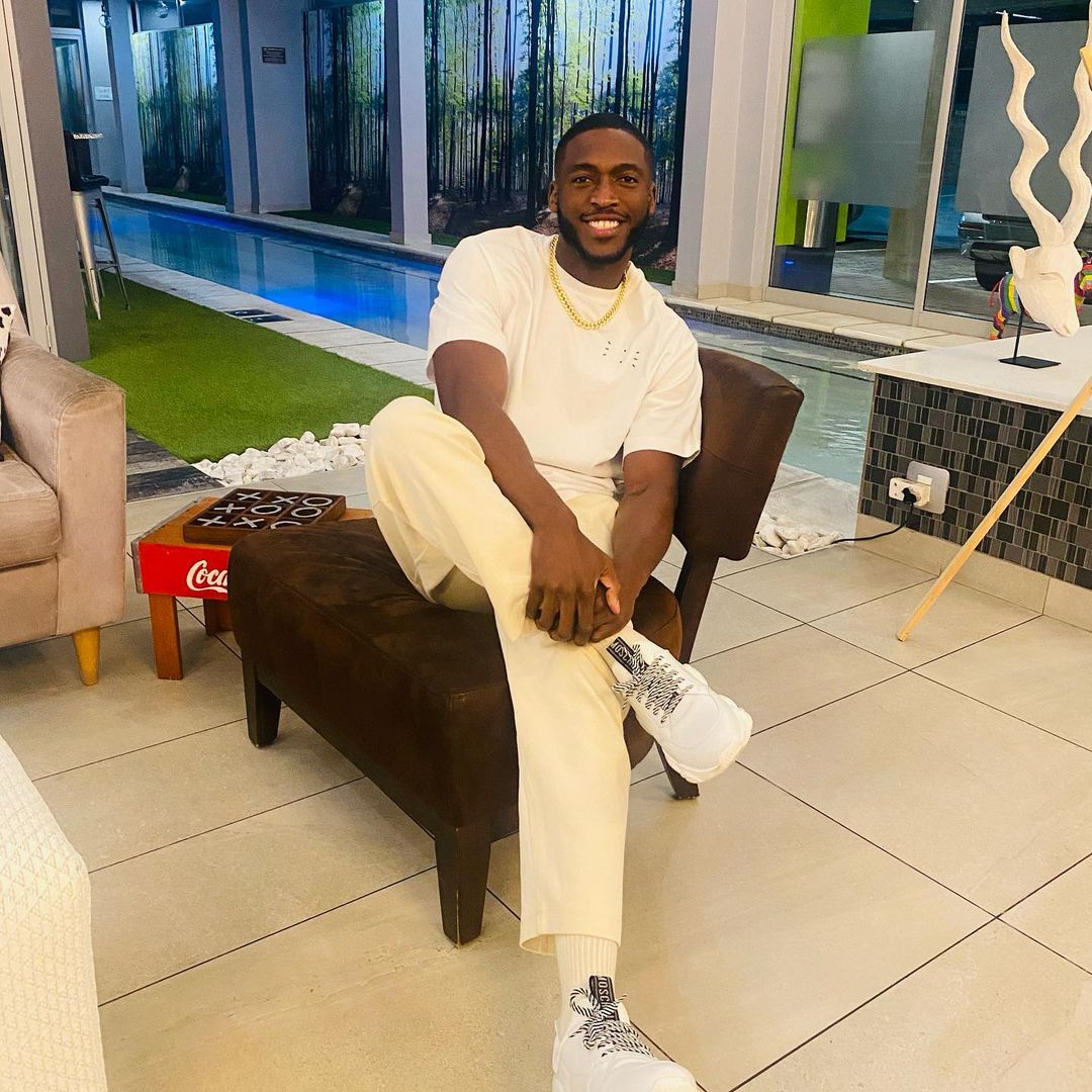 Daliwonga Motiwane sitting on a sofa in white t-shirt and cream trouser