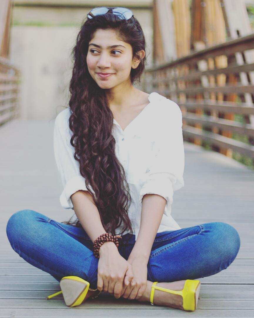 Sai Pallavi sitting on a bridge in white top and blue jeans