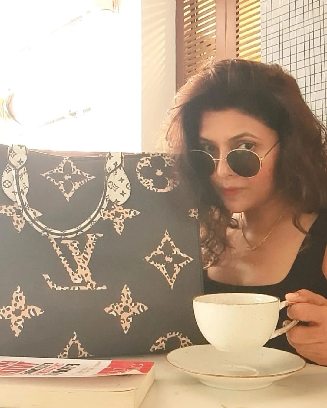 Luviena Lodh with a black hand bag and a cup of tea in hand