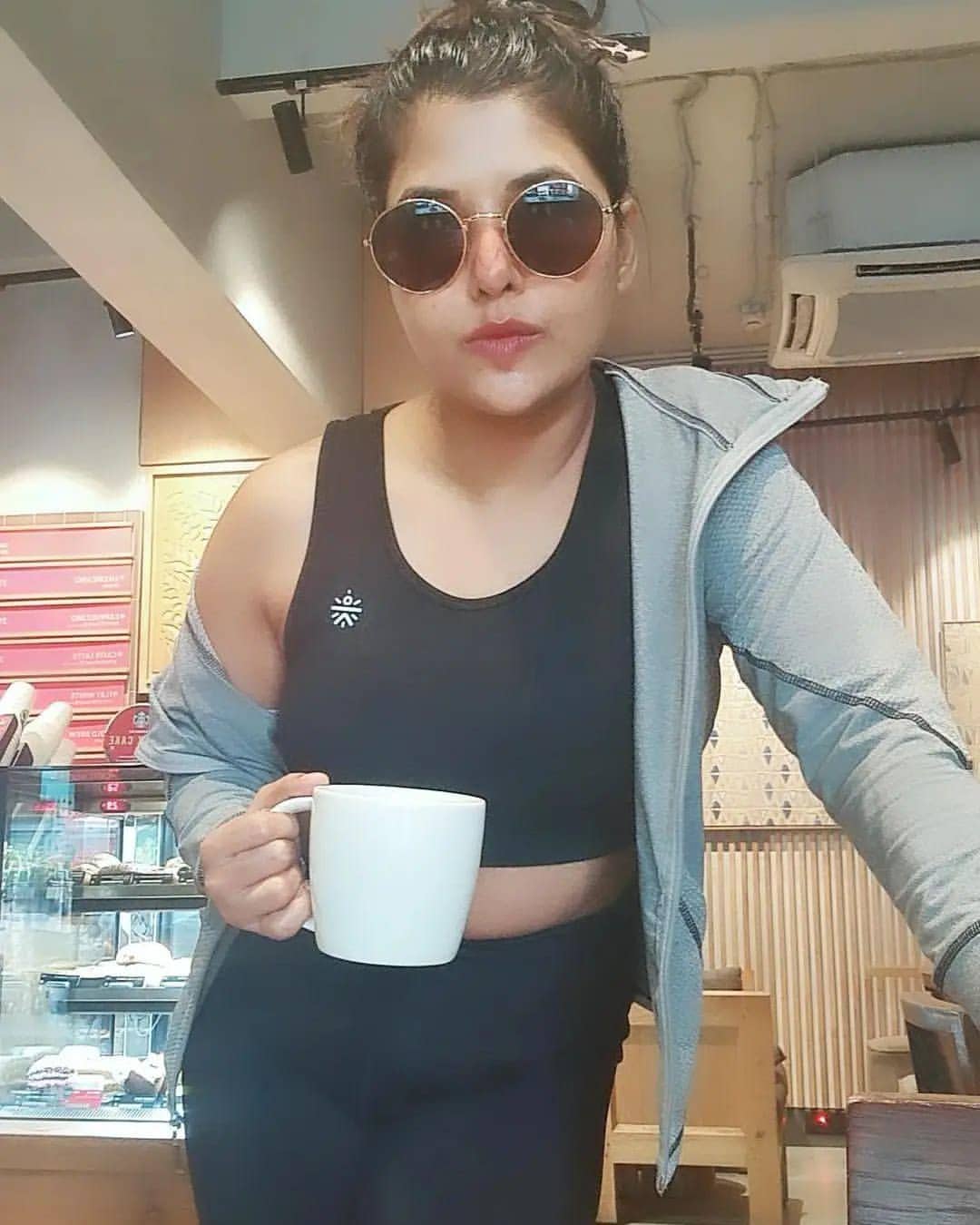 Luviena Lodh in black athleisure with a white cup in hand