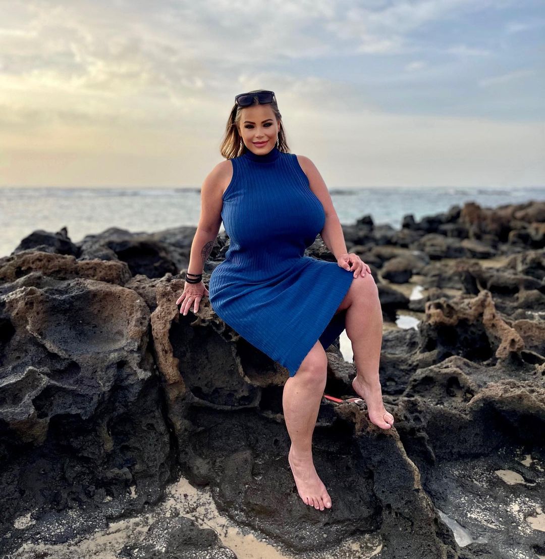 Bella Bodhi in high neck dark blue dress sitting on a rock at a beach