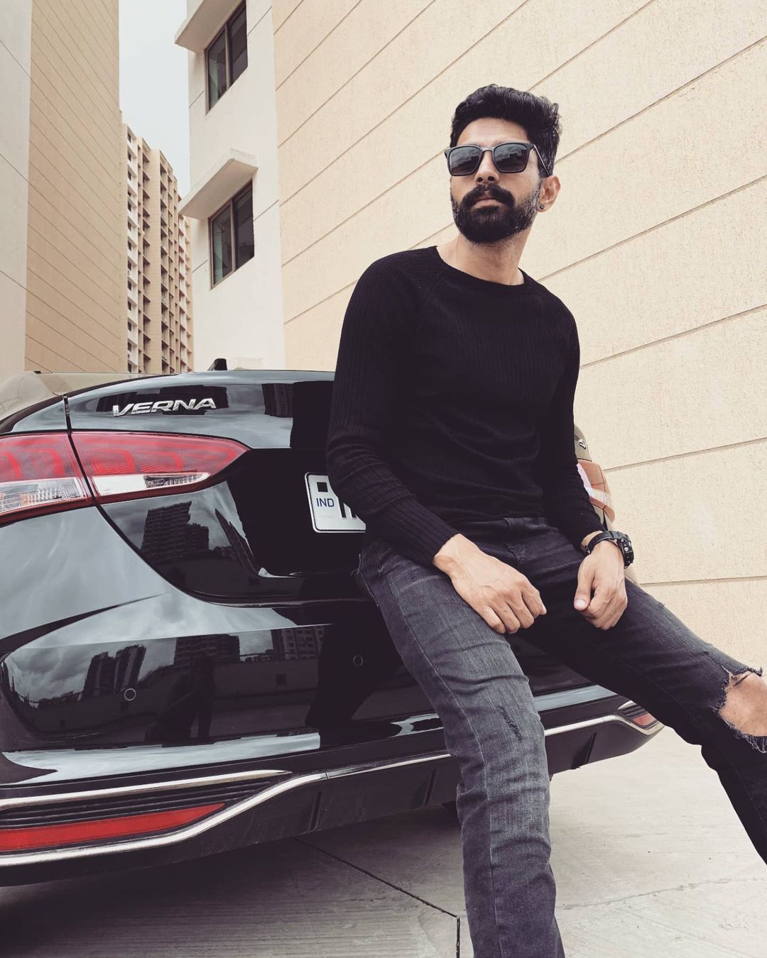 Abhishek Iyer sitting on the backside of a black verna in black outfit