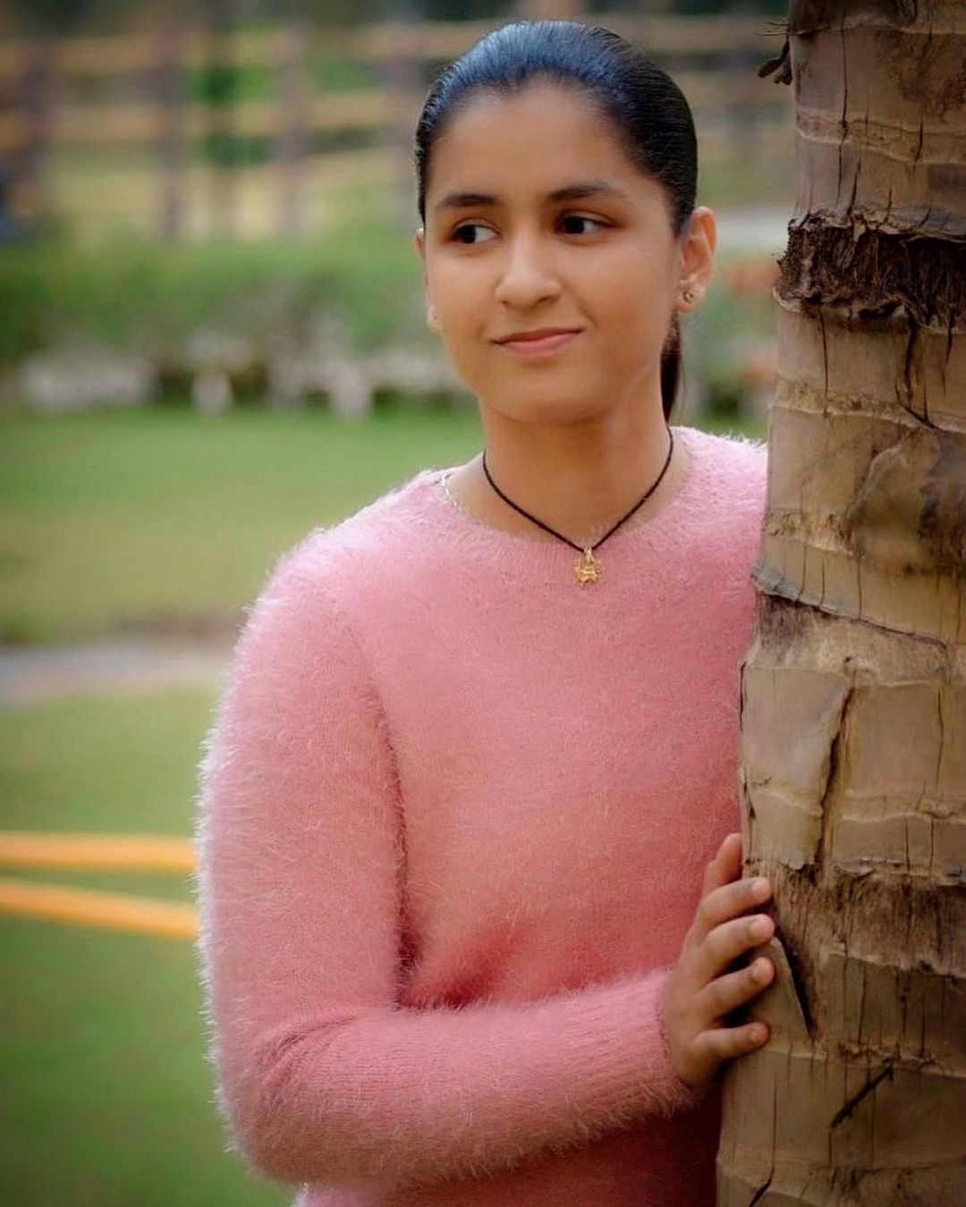 Naina Jaiswal in light pink sweater standing with a tree