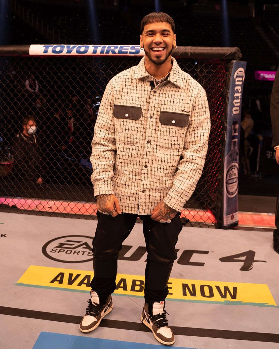 Anuel AA in cream shirt and black pants in a UFC ring