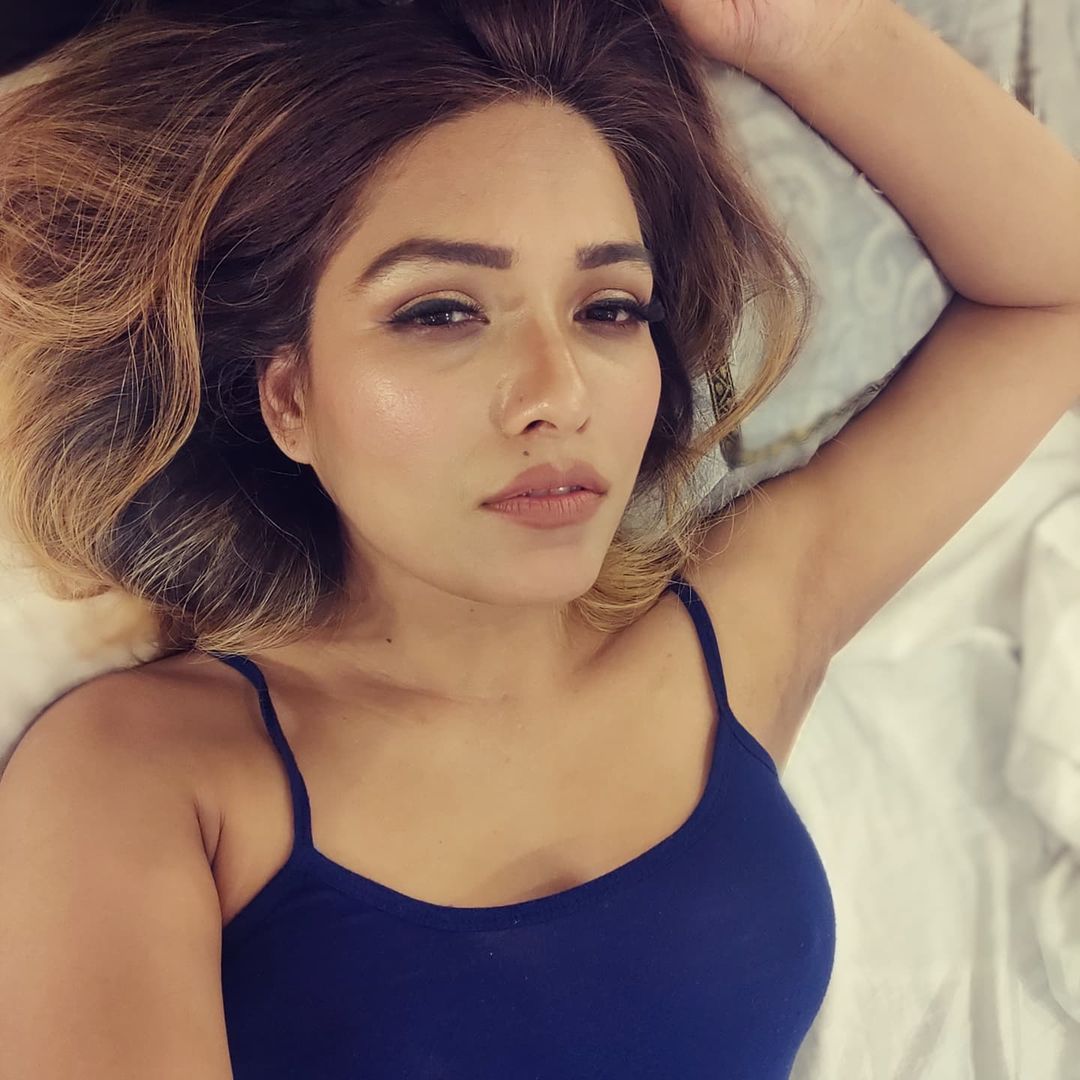 Zoya Rathore lying on a bed in a navy blue top 