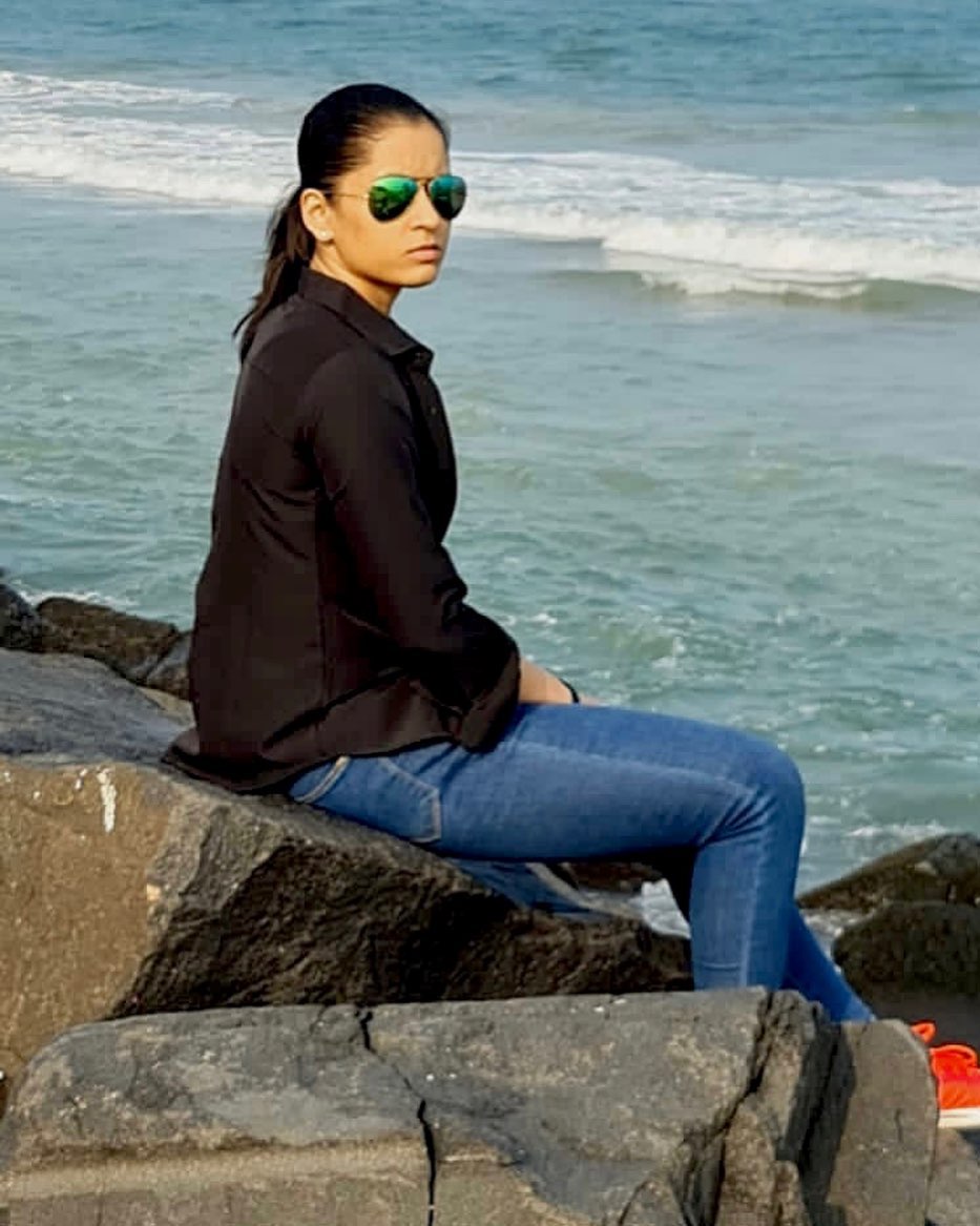 Naina Jaiswal sitting on a rock in black shirt and blue jeans
